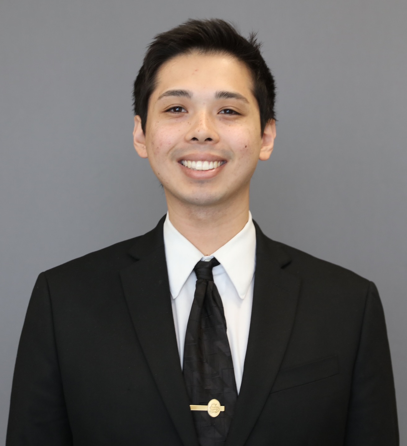 Porträt lächelnder Mann, kurze, schwarze Haare, weißes Hemd, schwarzes Sakko, schwarze Krawatte