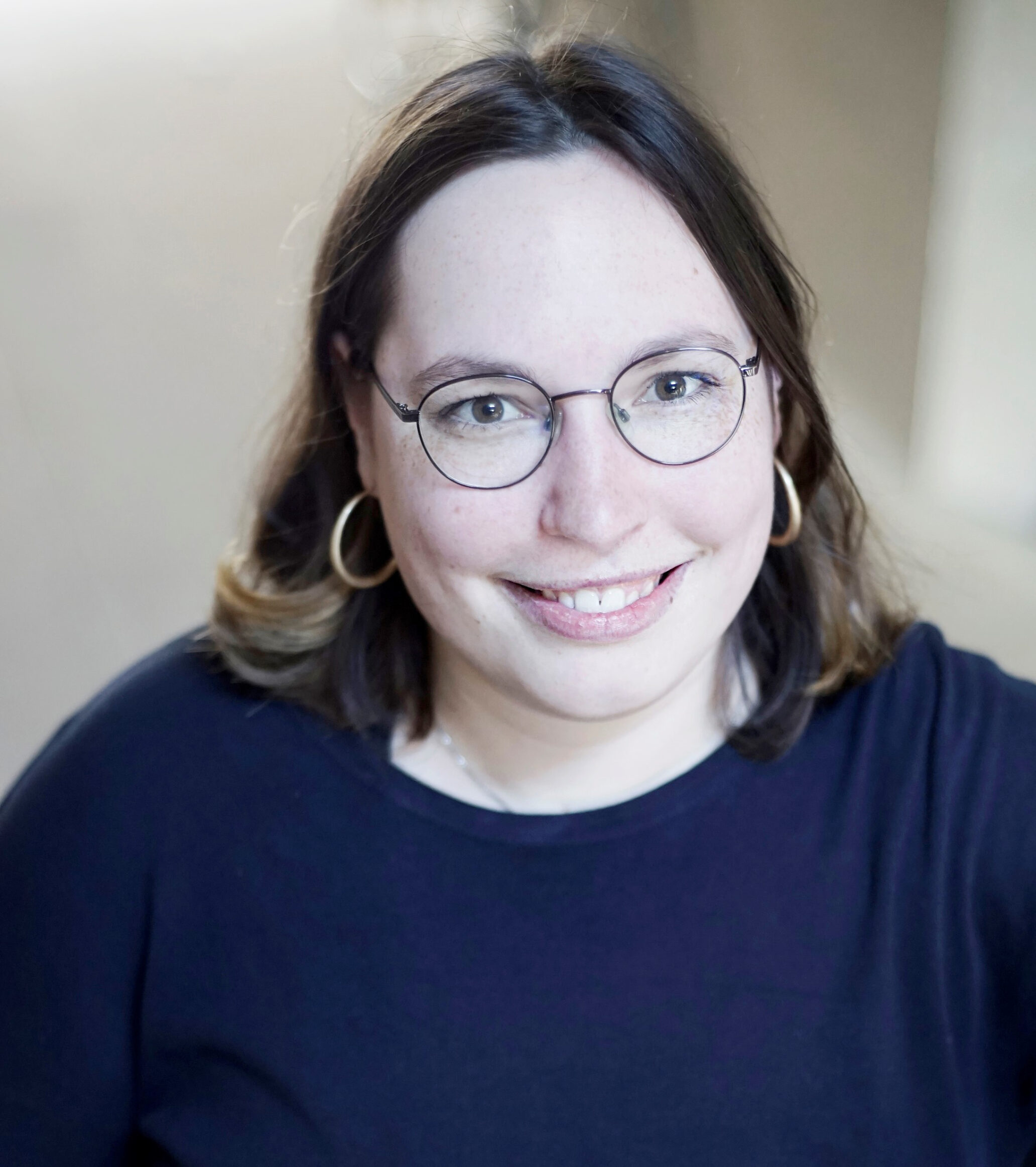 Person mit mittellangen Haaren, Ohrringen und Brille.