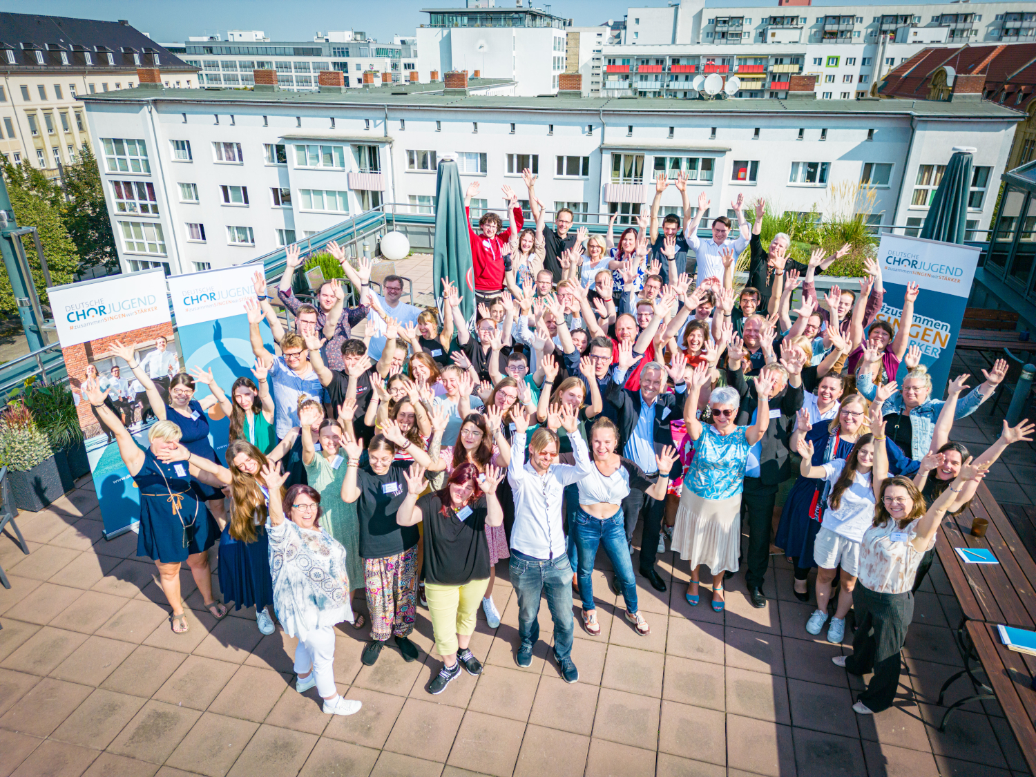 Großgruppenfoto, von oben fotografiert, die Personen winken mit beiden Armen.