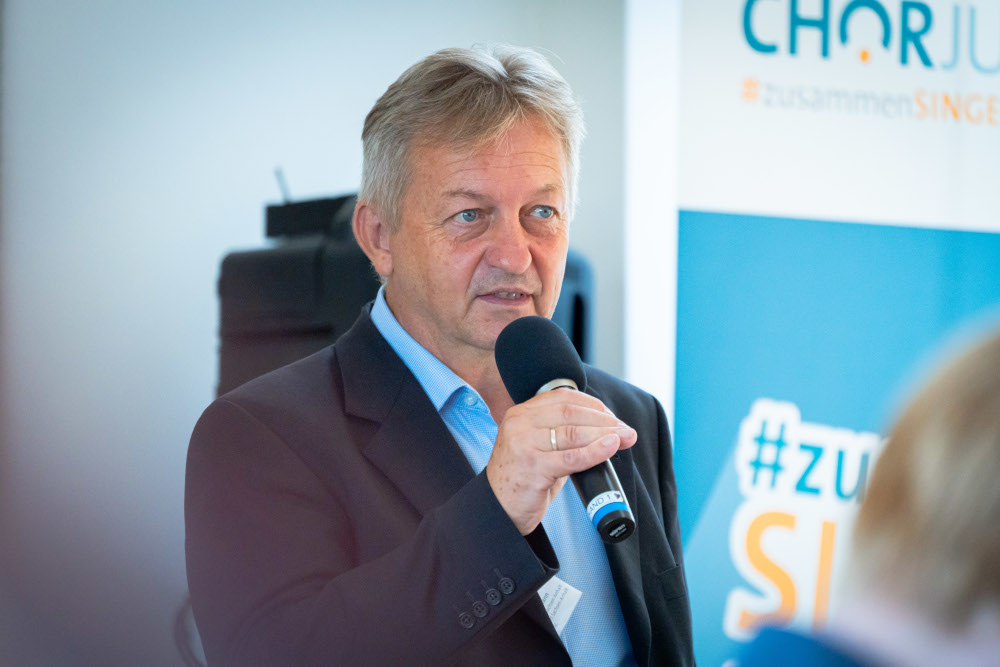 Mann im Jackett der in ein Mikrofon spricht.