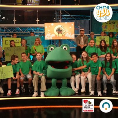 Eine Gruppe von Kindern mit grünen T-Shirts und einem großen Stoff-Frosch in der Mitte.