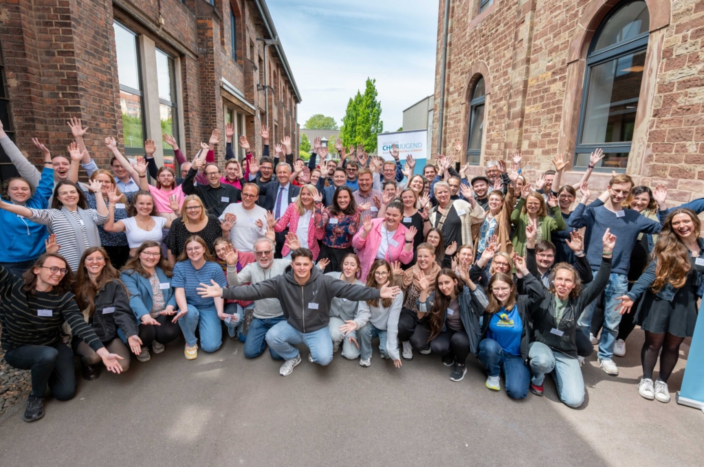 Gruppe von etwa 60 Personen draußen, die meisten heben die Arme hoch.