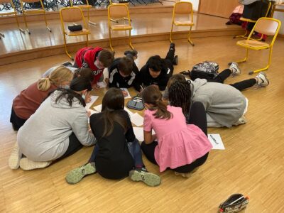 Kinder sitzen in einem Kreis auf dem Boden und schreiben etwas.