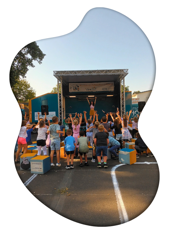 Singbus mit aufgeklappter Bühne, davor Kinder, die die Arme in die Luft reißen. Bild: Deutsche Chorjugend