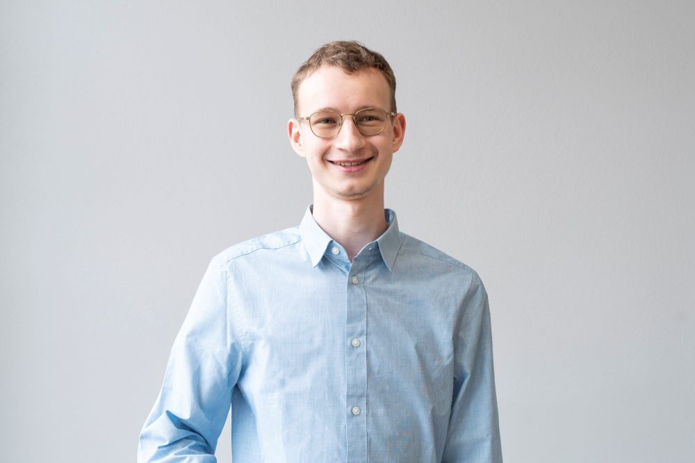 Portrait von Person mit kurzen Haaren, Brille und hellblauem Hemd